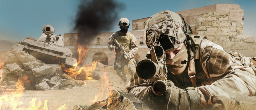 Photo of a fully equipped soldiers laying and aiming rifle on desert battlefield with running soldiers and tank