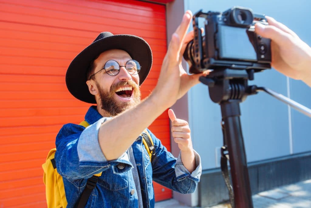 social media influencer personality creating content. man shooting video of himself using camera on tripod. Smiling bearded hipster singer communicating with subscribers outdoor interview concept.