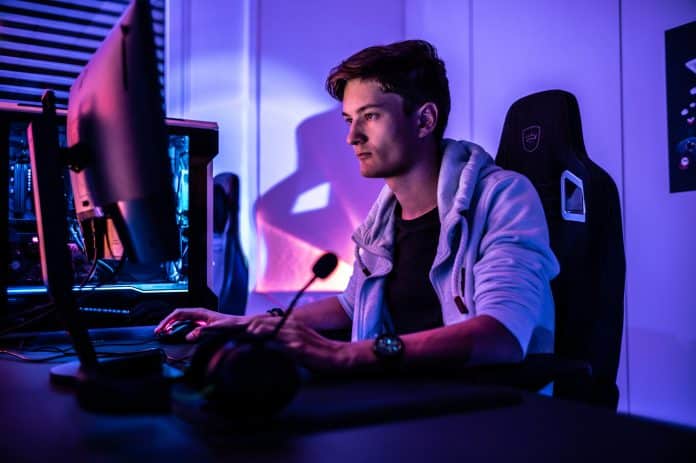 profile view of man sitting at desk bathed in purple light looking at computer screen