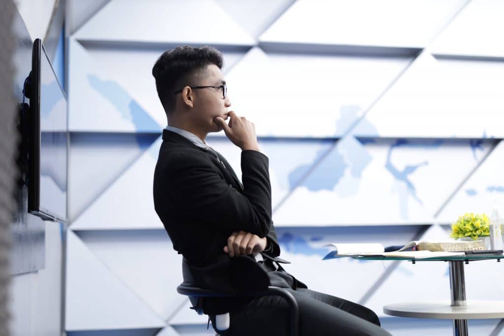 profile view of man wearing glasses sitting at glass desk pondering thought in office building