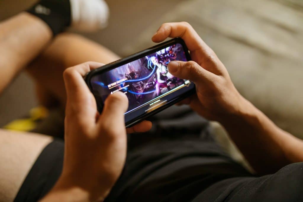 Man holding a mobile phone playing a mobile video game with crossed legs in blurred background